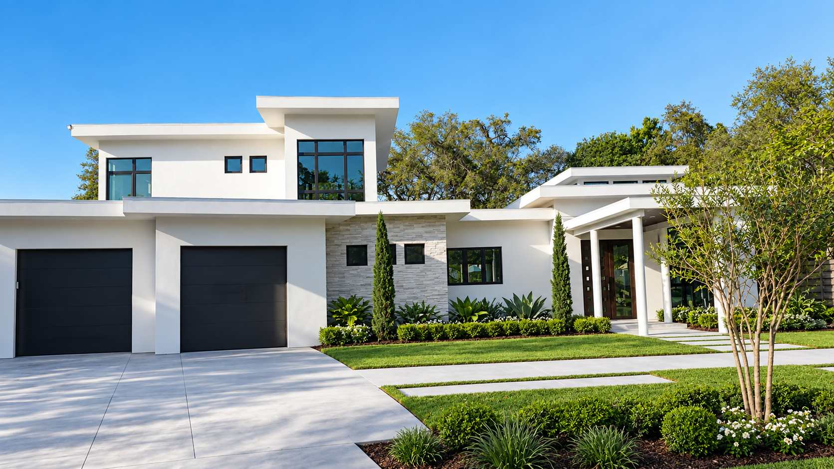 Two-story modern white stucco home in Sarasota, FL with flat rooflines, stacked stone accent wall, black-framed windows, and two-car garage